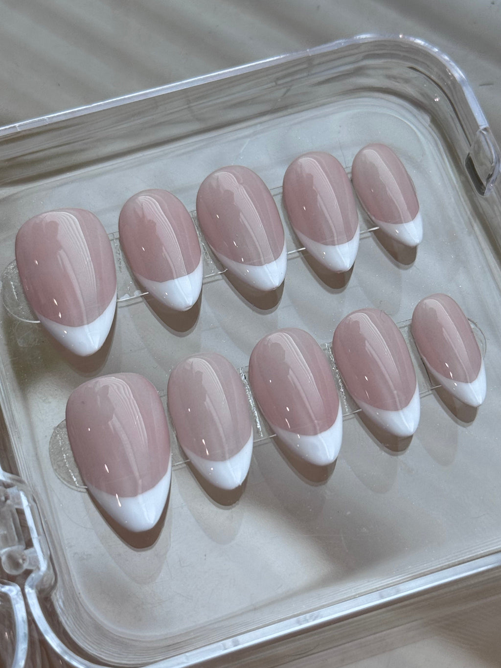 A set of ten press-on nails with a classic French manicure design, featuring a dusty pink base and white tips, displayed inside a clear plastic case.